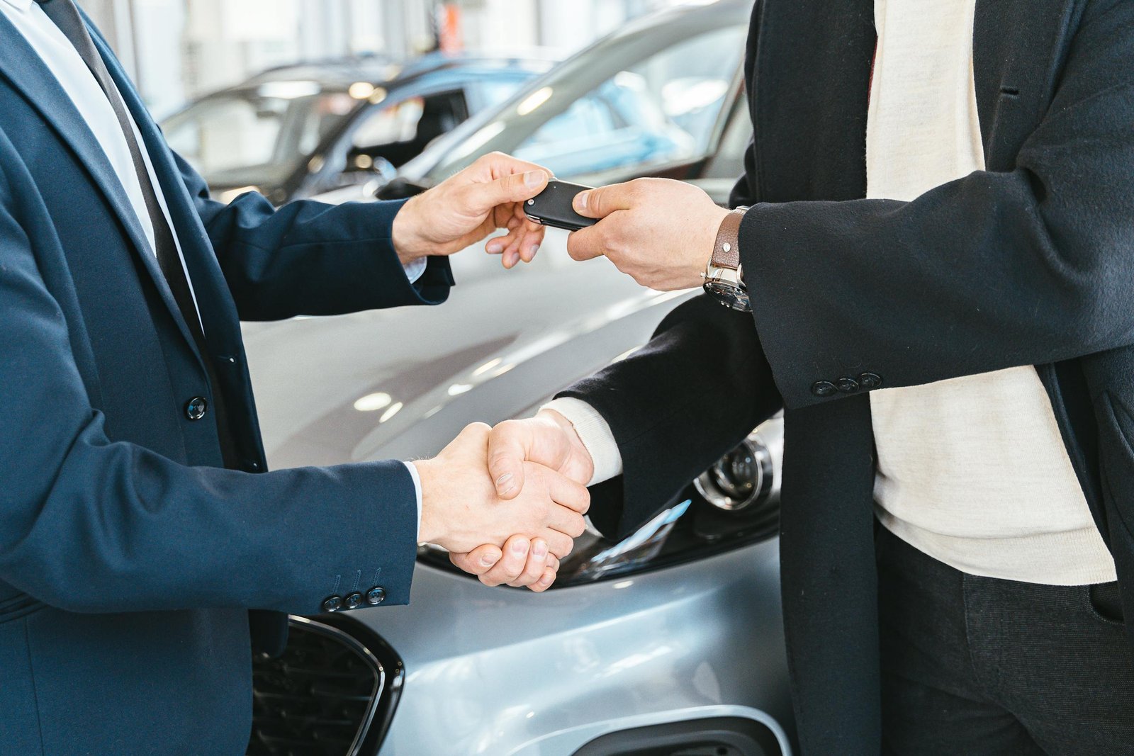 Two businessmen shaking hands and exchanging car keys in a dealership. Symbolizes a successful deal.