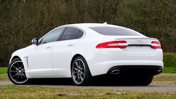 A sleek white Jaguar XF sedan parked outdoors with alloy wheels on a country road.