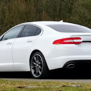 A sleek white Jaguar XF sedan parked outdoors with alloy wheels on a country road.