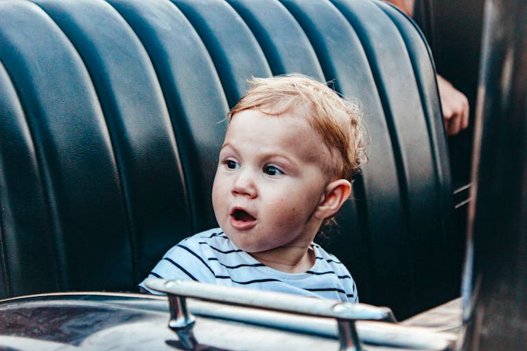 Cute child with surprised expression sitting in a car seat wearing a striped shirt.