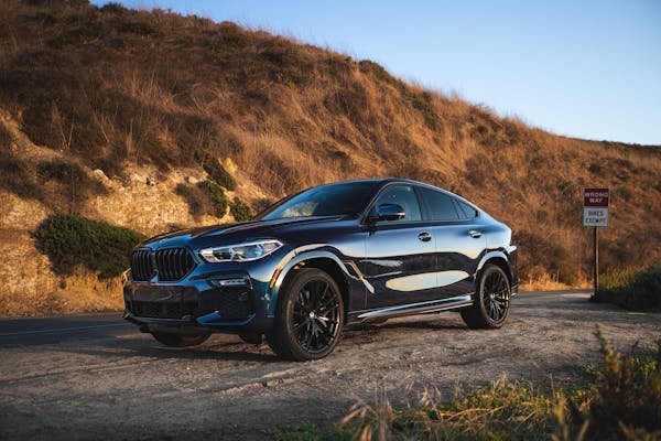 Elegant black BMW SUV parked on a scenic dirt road in Newport Beach, capturing the sunset glow.