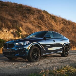 Elegant black BMW SUV parked on a scenic dirt road in Newport Beach, capturing the sunset glow.