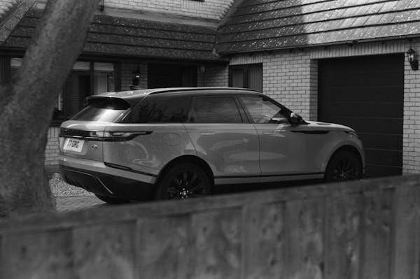 Monochrome image of a Range Rover Velar parked in a suburban driveway.