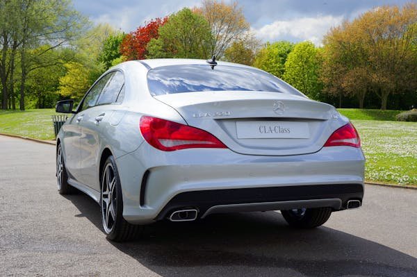 Rear view of a sleek silver Mercedes CLA-Class parked in a lush green park during fall.