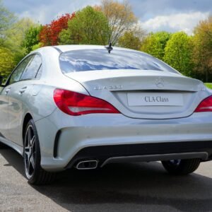 Rear view of a sleek silver Mercedes CLA-Class parked in a lush green park during fall.